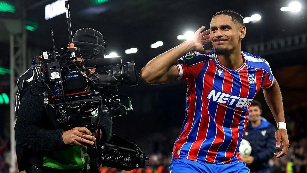 Crystal Palace's Maxence Lacroix cups his right ear with his right hand as he stands next to a TV camera